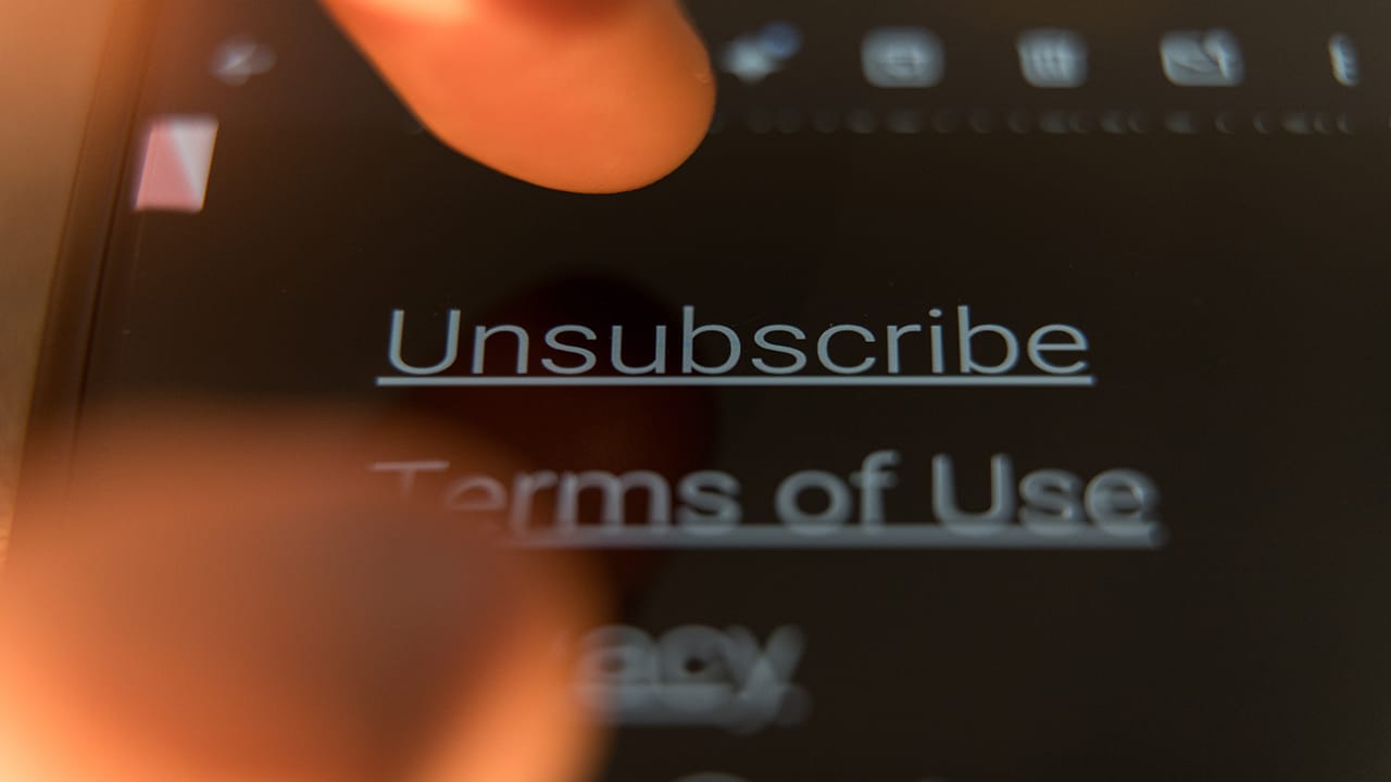 Finger pressing unsubscribe button on smartphone screen, illustrating subscription cancellation dark patterns